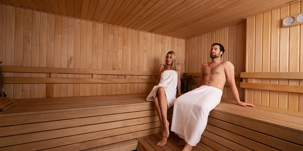 individueller Saunabau, Mann und Frau sitzen in einer Sauna mit Handtuch, genießen die wohltuende Wärme, Art of Spa